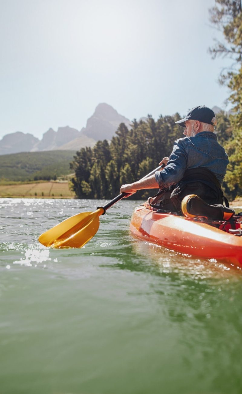 Rear view of a mature man canoeing in a lake. Senior man paddling kayak on a summer day.